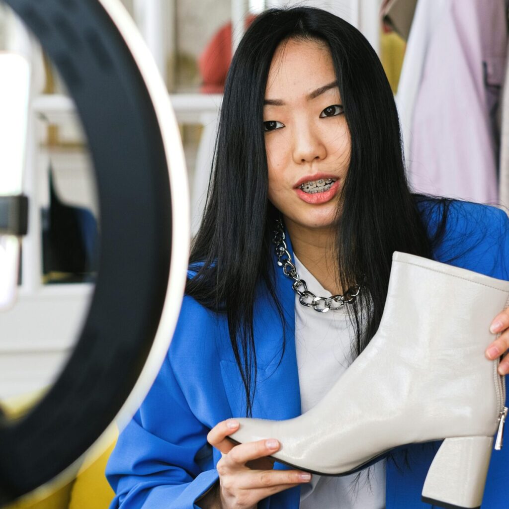 Young woman fashion vlogger recording a video about stylish white boots indoors.